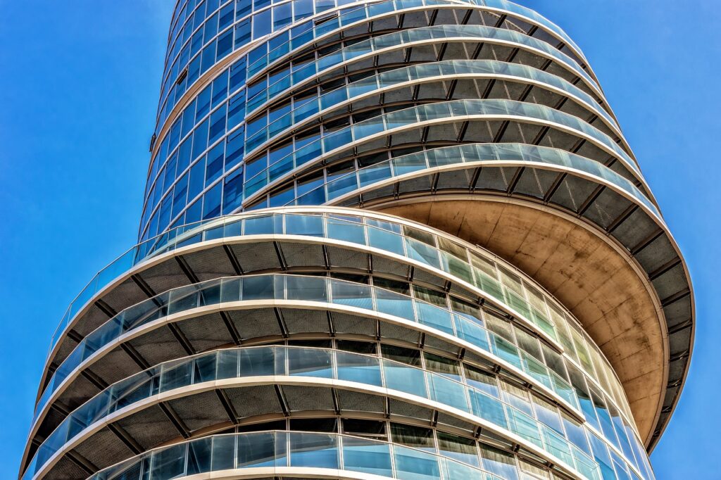 Vue en contre-plongée d’un immeuble moderne en verre aux lignes courbes, sous un ciel bleu