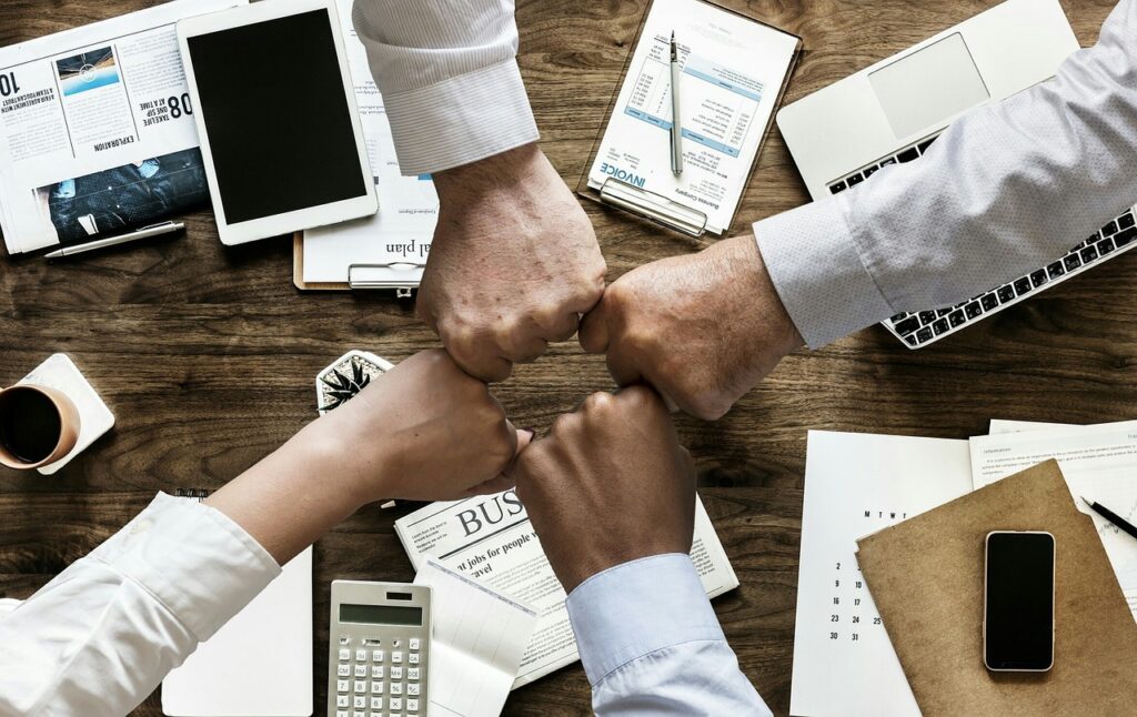 Quatre personnes se saluant par un geste de poing au-dessus d’un bureau couvert de documents, symbolisant l’esprit d’équipe en milieu professionnel.