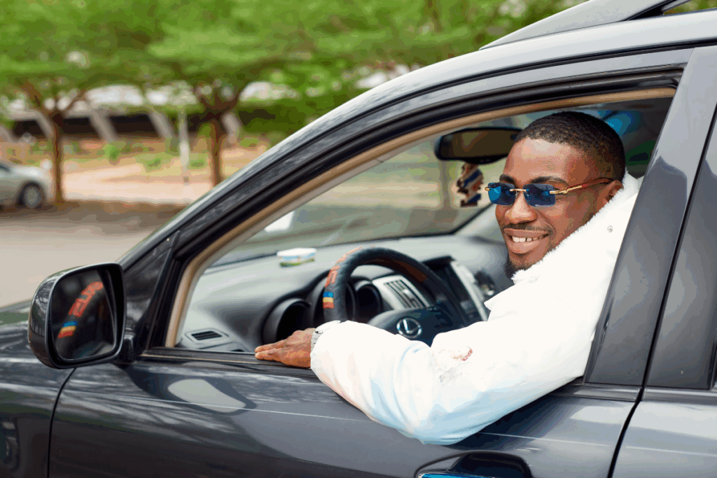 Homme souriant au volant d’une voiture, regardant vers l’extérieur par la fenêtre ouverte.