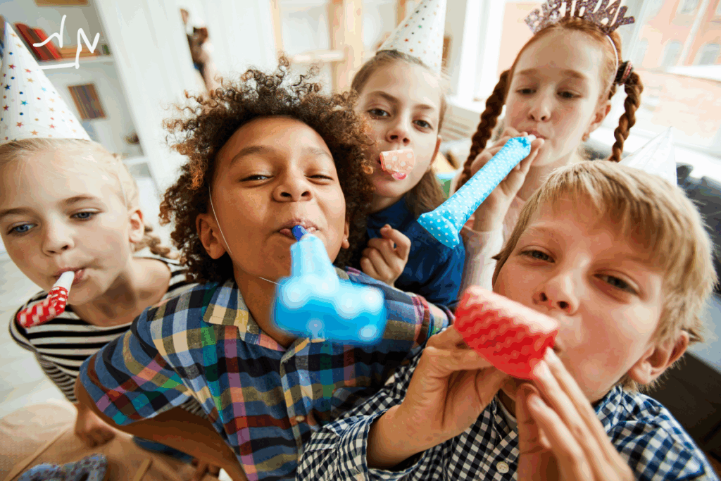 Groupe d’enfants portant des chapeaux de fête, soufflant des serpentins et s’amusant lors d’un anniversaire.